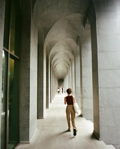 A person walking alone down a long colonnade of pale arches